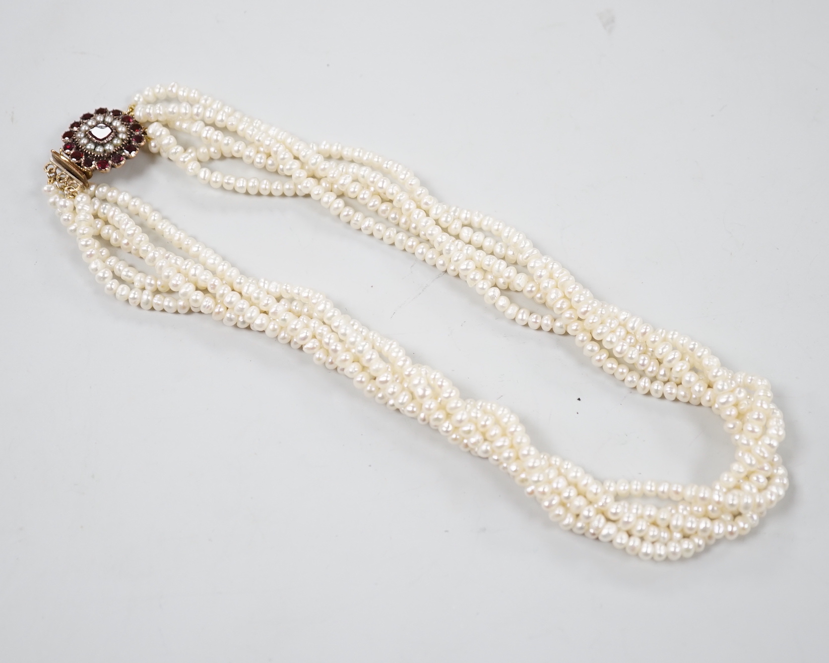 A cultured baroque pearl torsade choker necklace, with early yellow metal garnet and split pearl set clasp, 38cm.